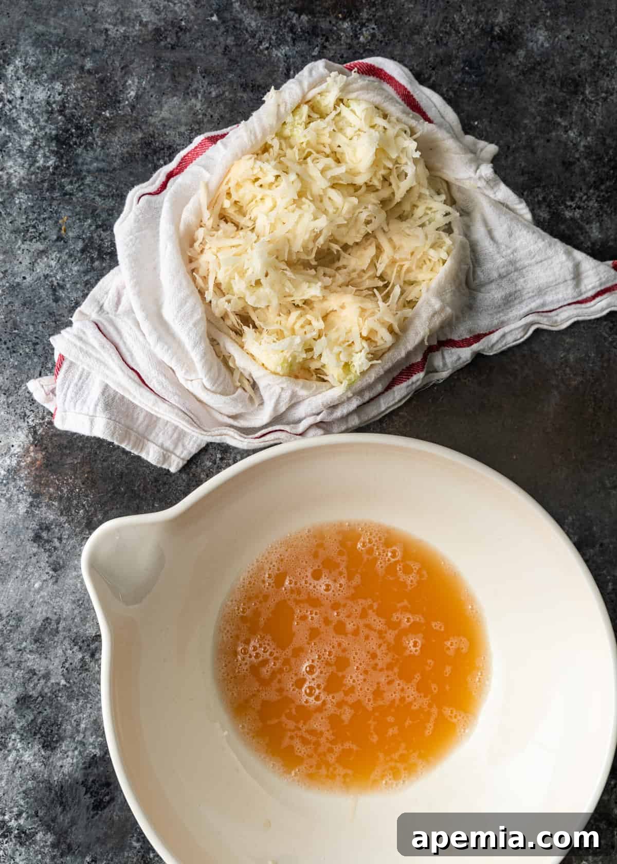 Overhead process shot demonstrating the crucial step of squeezing excess water from the shredded potato and onion mixture using a kitchen towel.