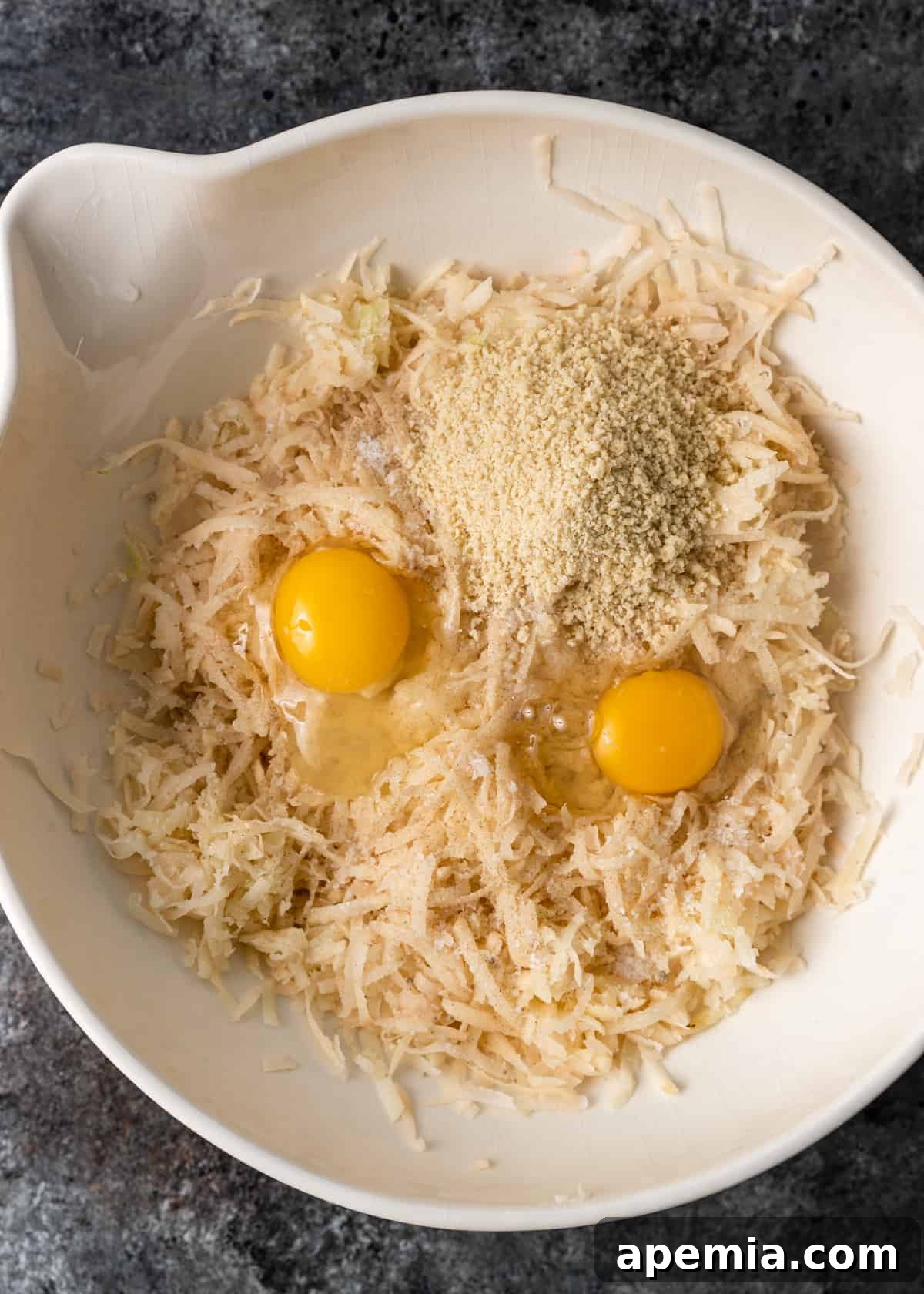Overhead process shot showing the shredded potato and onion mixture combined with panko breadcrumbs and eggs in a bowl, forming the latke batter.
