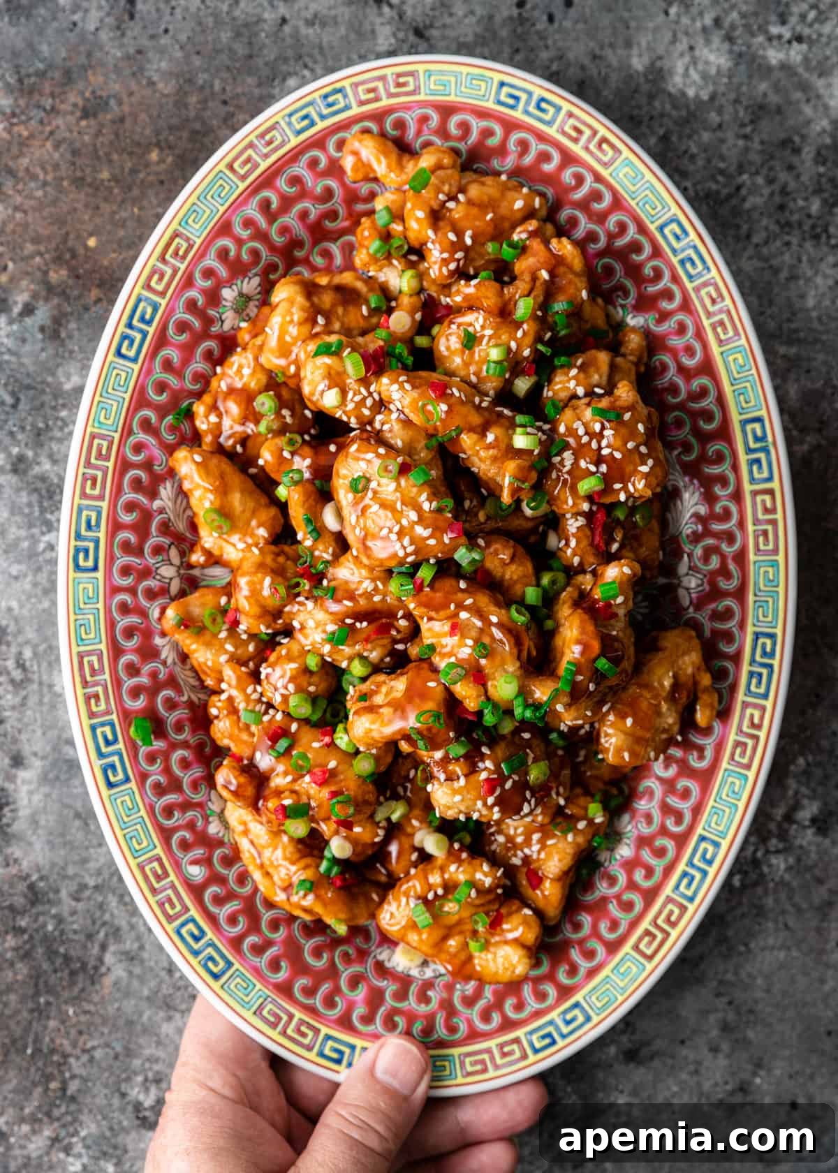 closeup overhead: hand holding ready to serve honey chicken on colorful plate