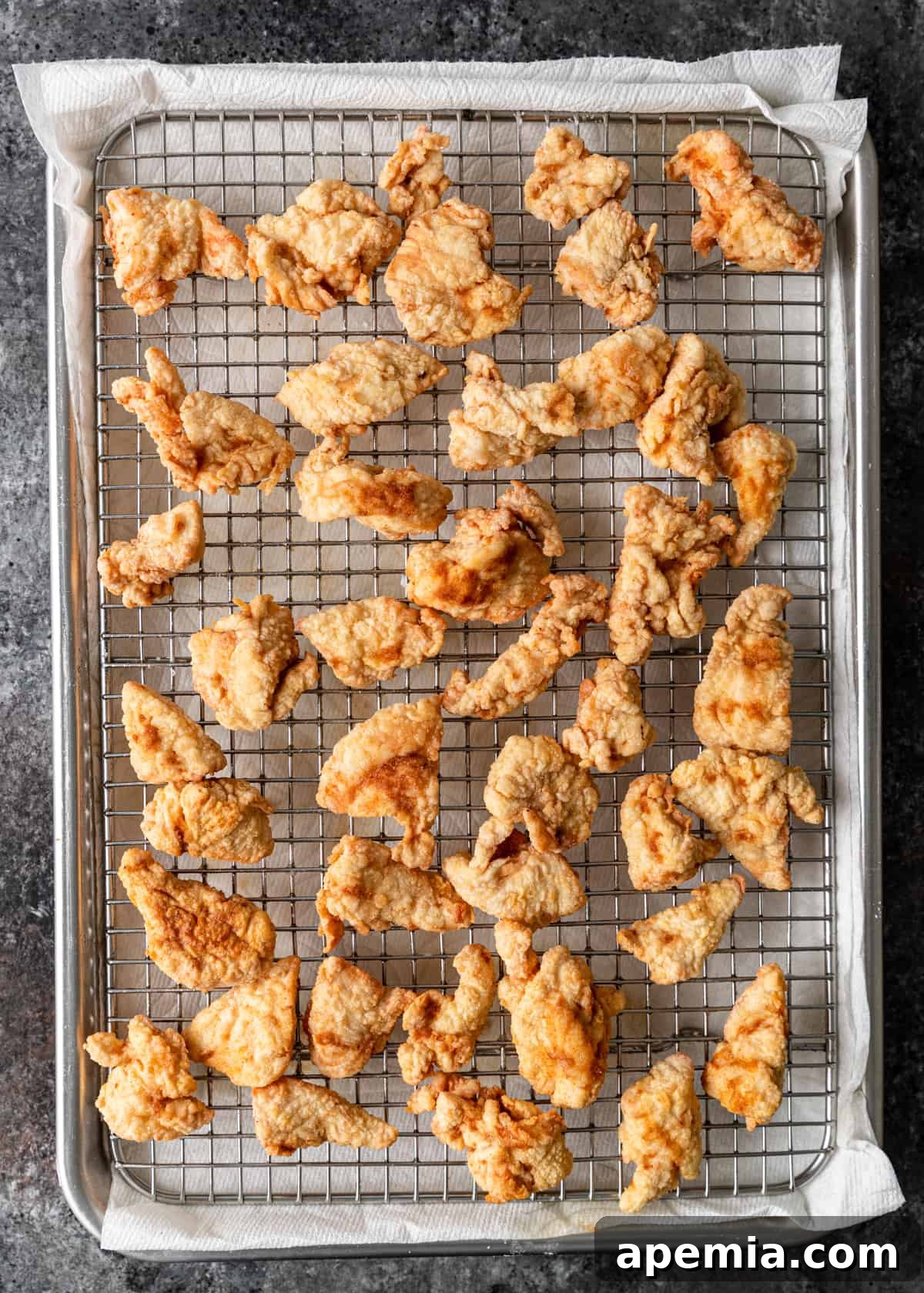 closeup overhead: draining fried chicken on cooling rack over paper towel on sheet pan
