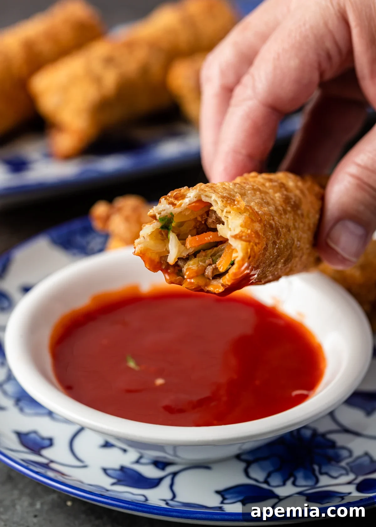 Perfectly Crispy Egg Rolls 3 closeup: hand holding egg roll dipped in sweet and sour sauce
