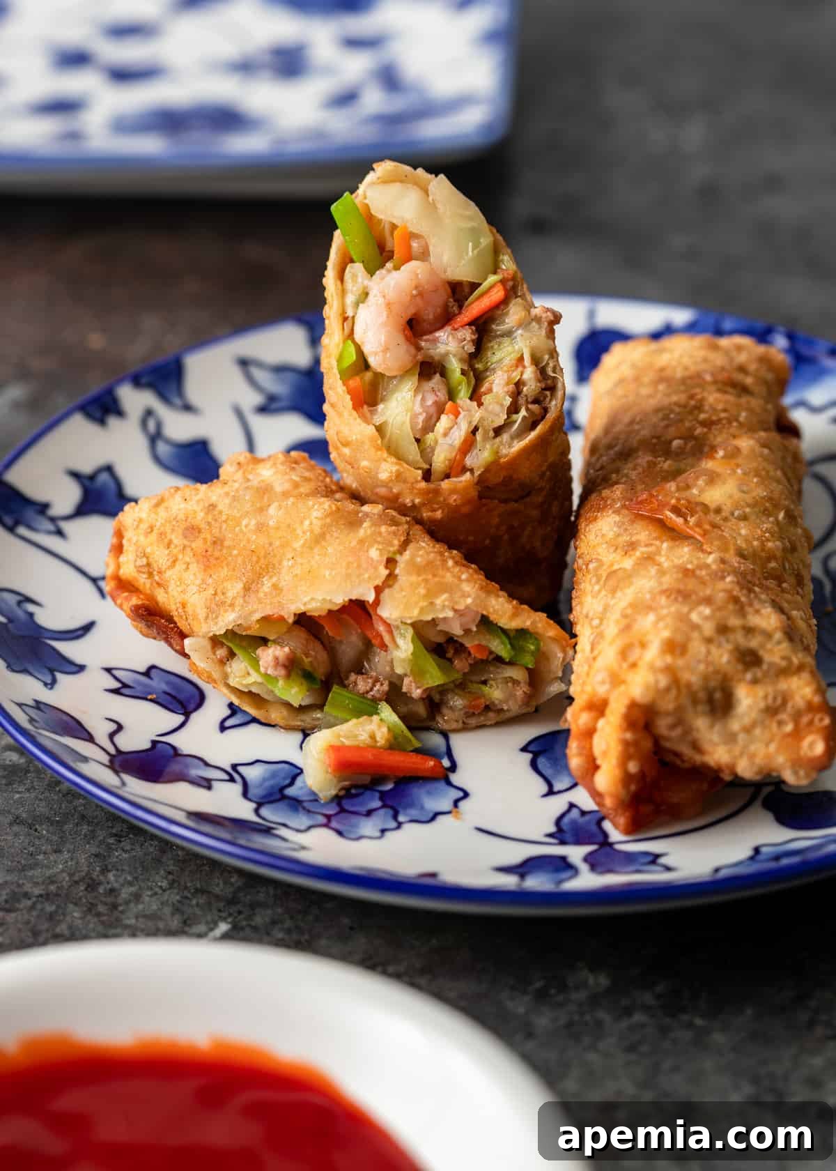Perfectly Crispy Egg Rolls 10 closeup side view: crispy egg rolls on a blue and white plate with side of sweet and sour sauce