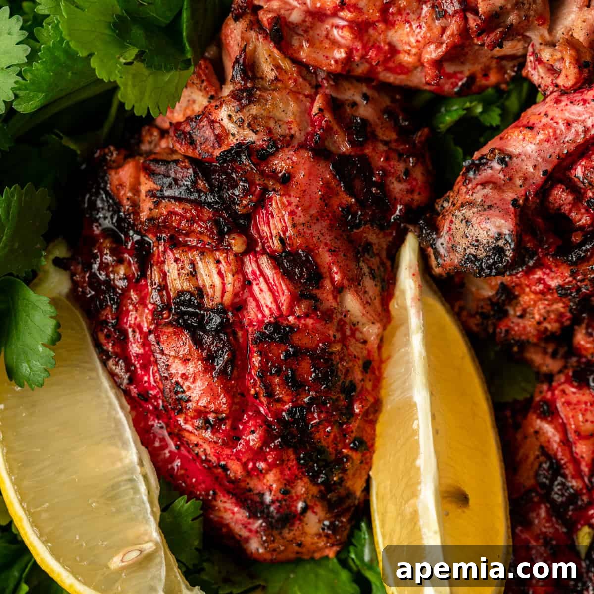Vibrantly colored Tandoori Chicken pieces garnished with cilantro and lemon wedges