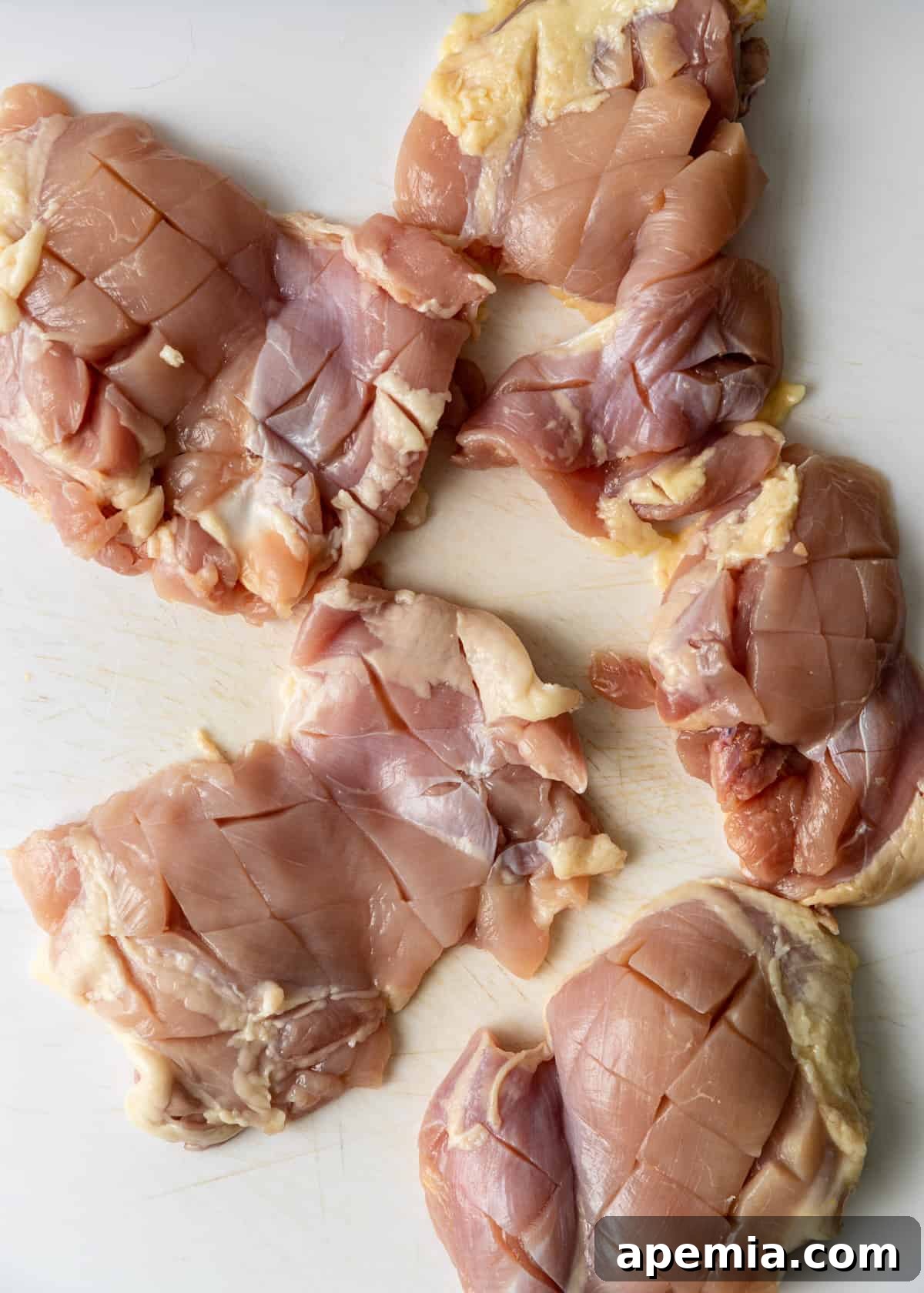 Chef making deep cuts into boneless chicken thighs to prepare for marinating