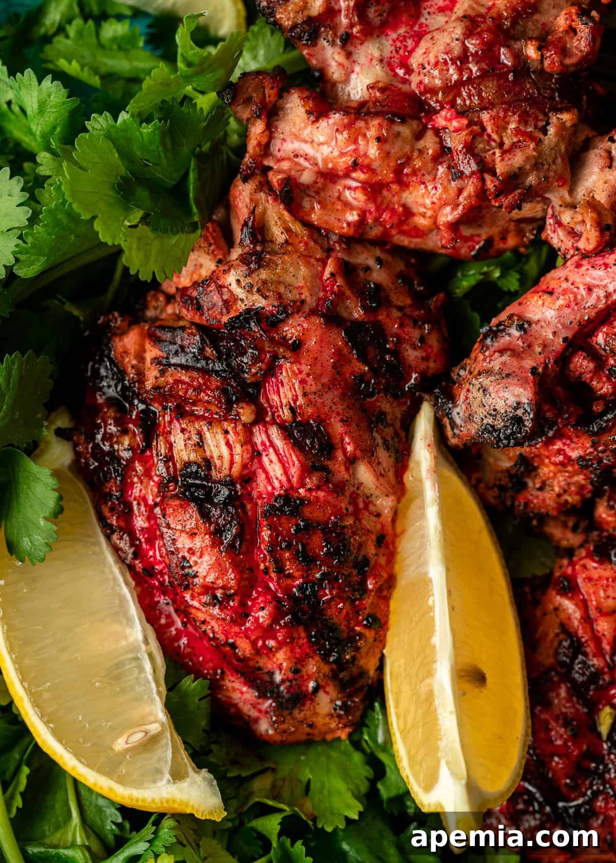 Platter of perfectly cooked Tandoori Chicken, garnished with fresh cilantro and vibrant lemon wedges