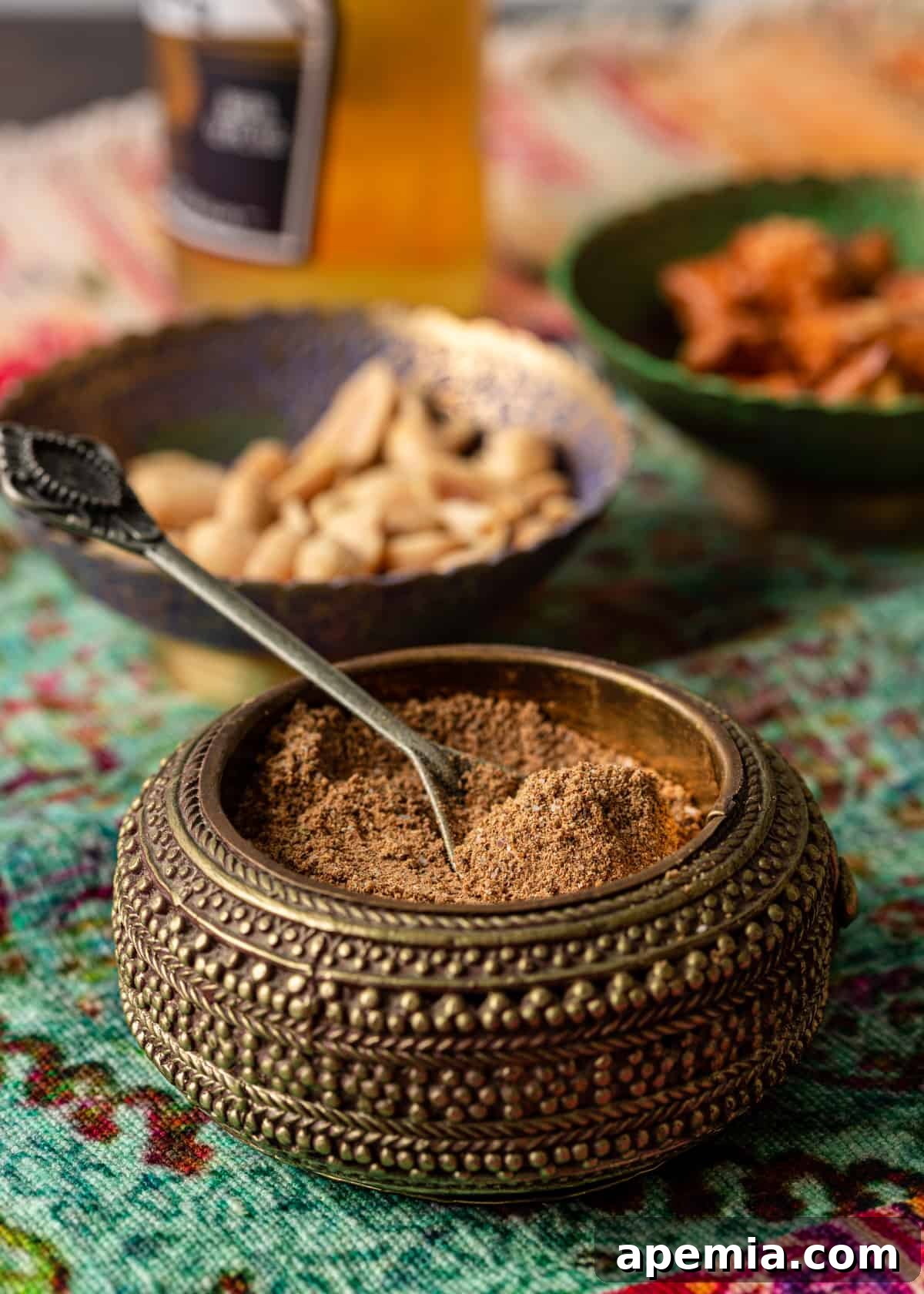 Close-up side view of fine chaat masala powder elegantly presented in a small bowl with a silver spoon, showcasing its granular consistency.
