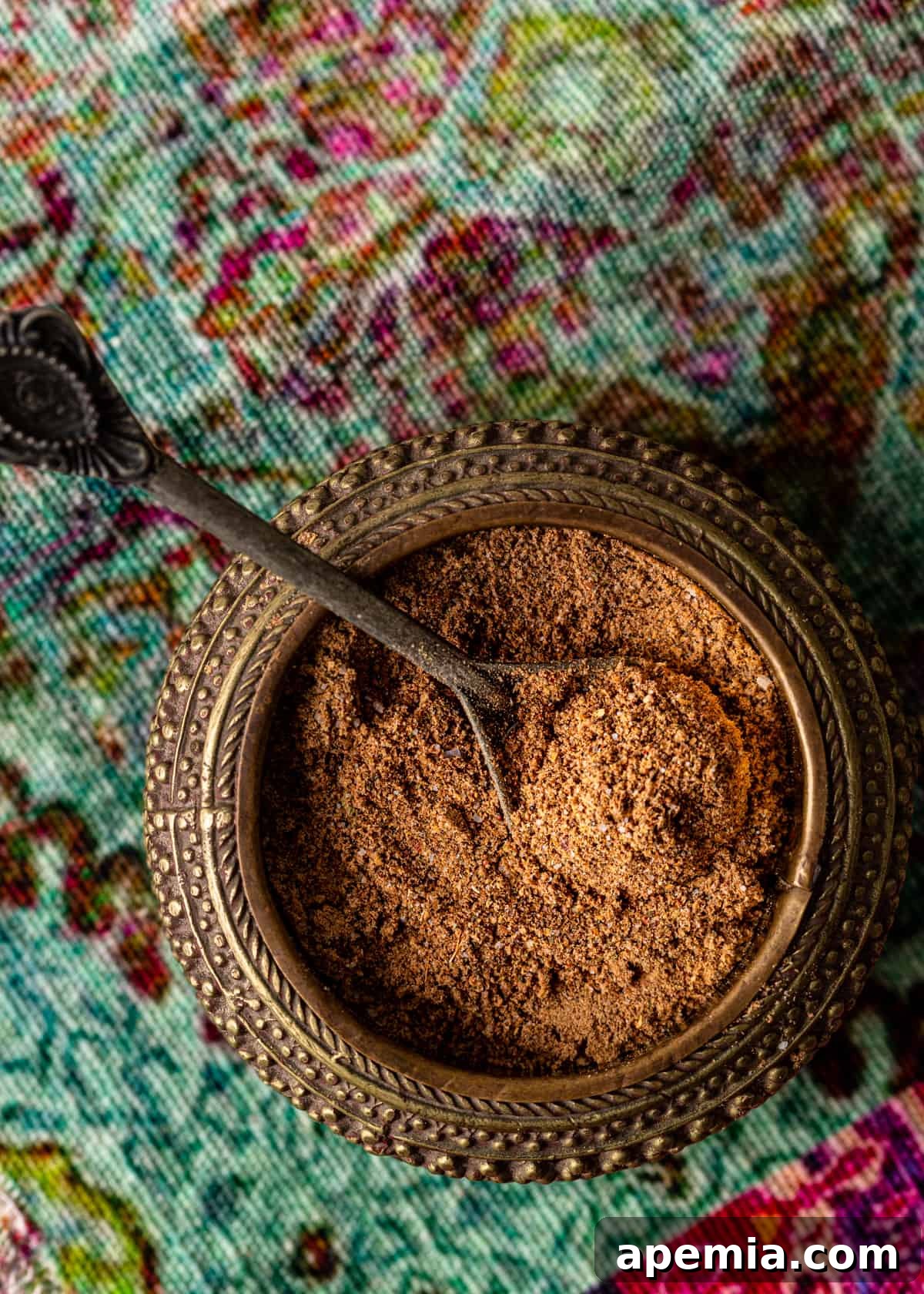 Overhead perspective of a bowl filled with fragrant chaat masala powder, accompanied by a small spoon, positioned perfectly for serving and enjoyment.