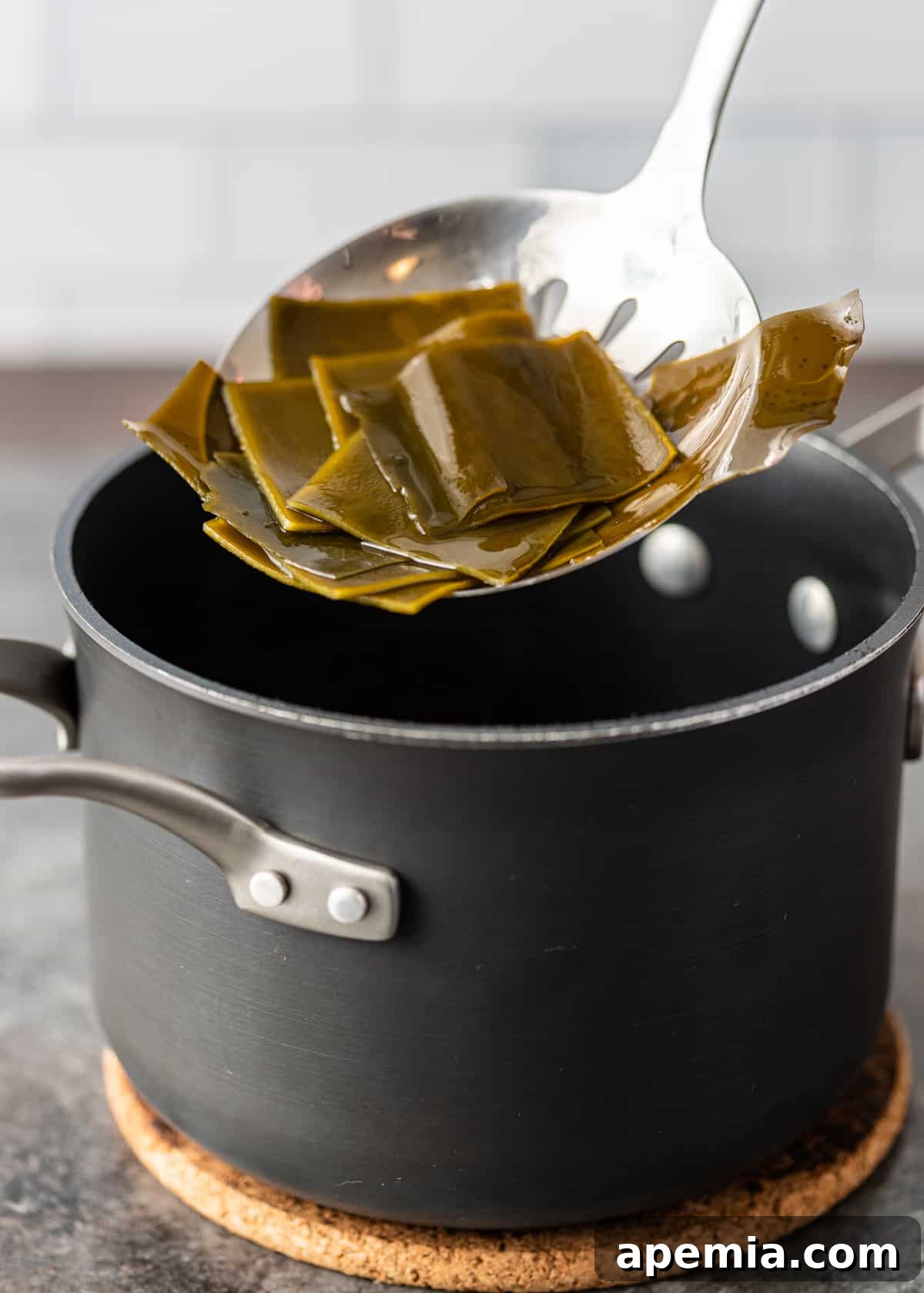 Removing cooked kombu (dried kelp) from a pot of water with tongs.