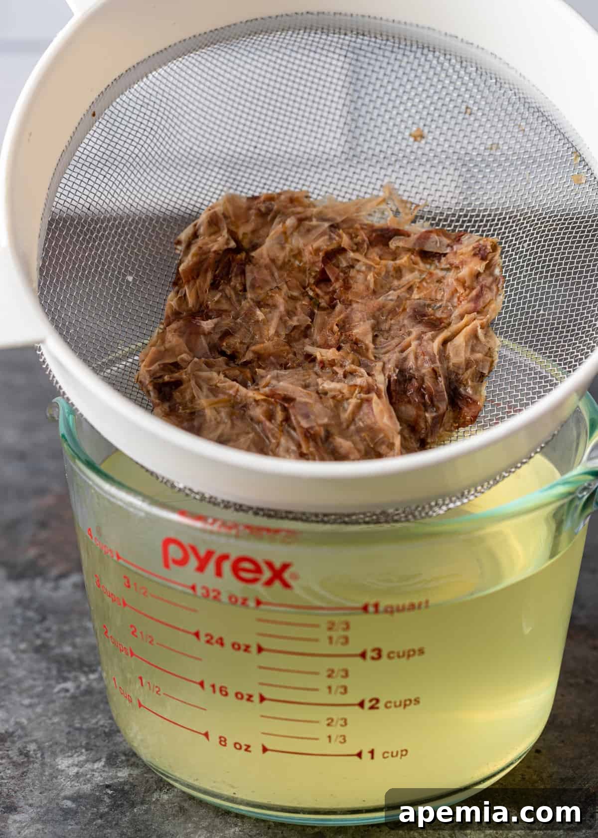 Straining dried bonito flakes through a fine-mesh sieve to create clear dashi.