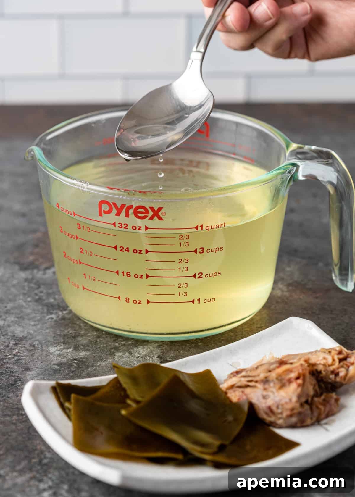 A spoon dipped into a measuring cup of golden Japanese soup stock (dashi).