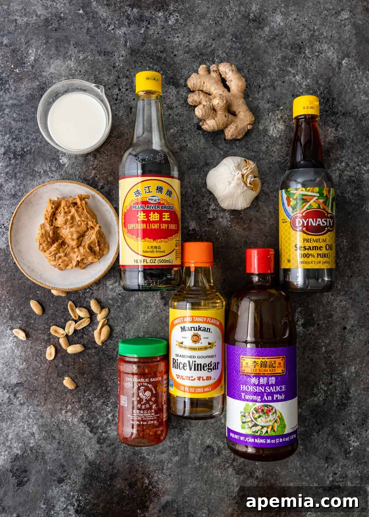 A selection of fresh ingredients laid out, including peanut butter, soy sauce, milk, chili paste, sesame oil, rice vinegar, hoisin sauce, sugar, ginger, and garlic, ready to be transformed into peanut sauce.