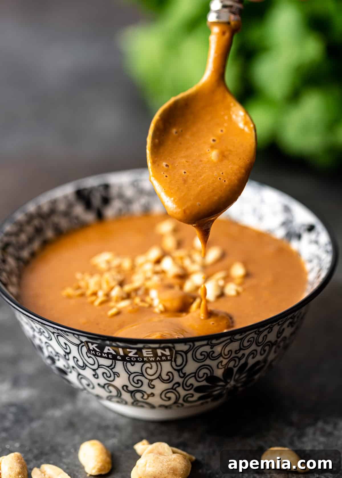 A spoon dripping with rich, creamy peanut sauce, showcasing its luscious texture.