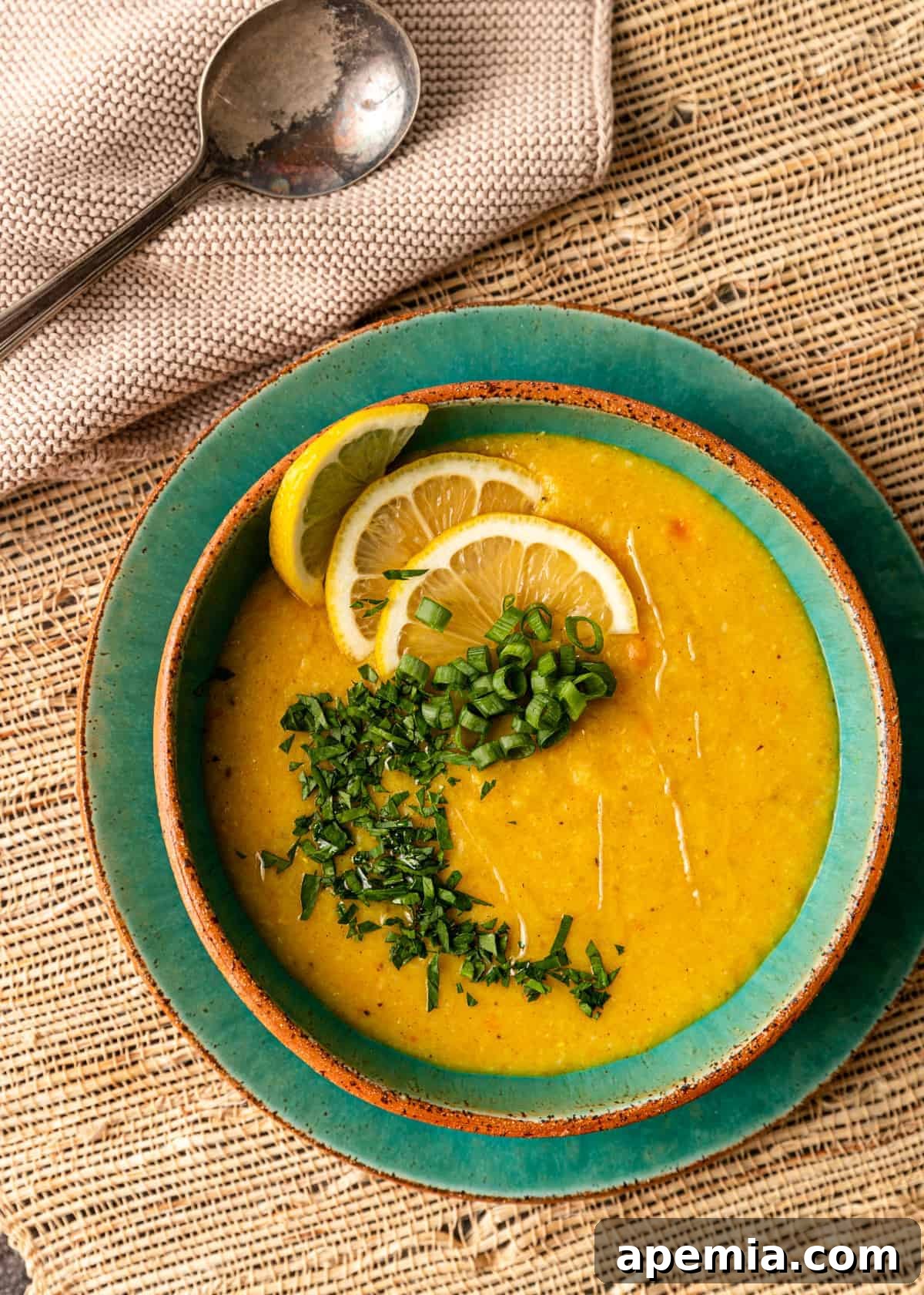 overhead: bowl of thick yellow soup garnished with scallion and lemon slices