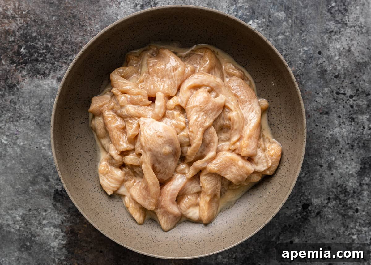 Cornstarch and oil being added to marinated chicken, creating a protective coating.