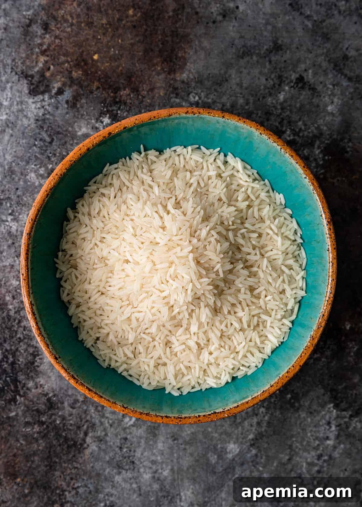 A close-up shot of dry, uncooked jasmine rice grains in a rustic bowl, showcasing its pristine, long-grain quality before preparation.