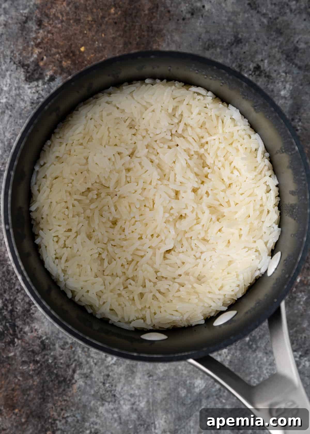 A close-up view of jasmine rice simmering gently in a saucepan on the stovetop, covered, steam subtly escaping, indicating perfect cooking conditions.