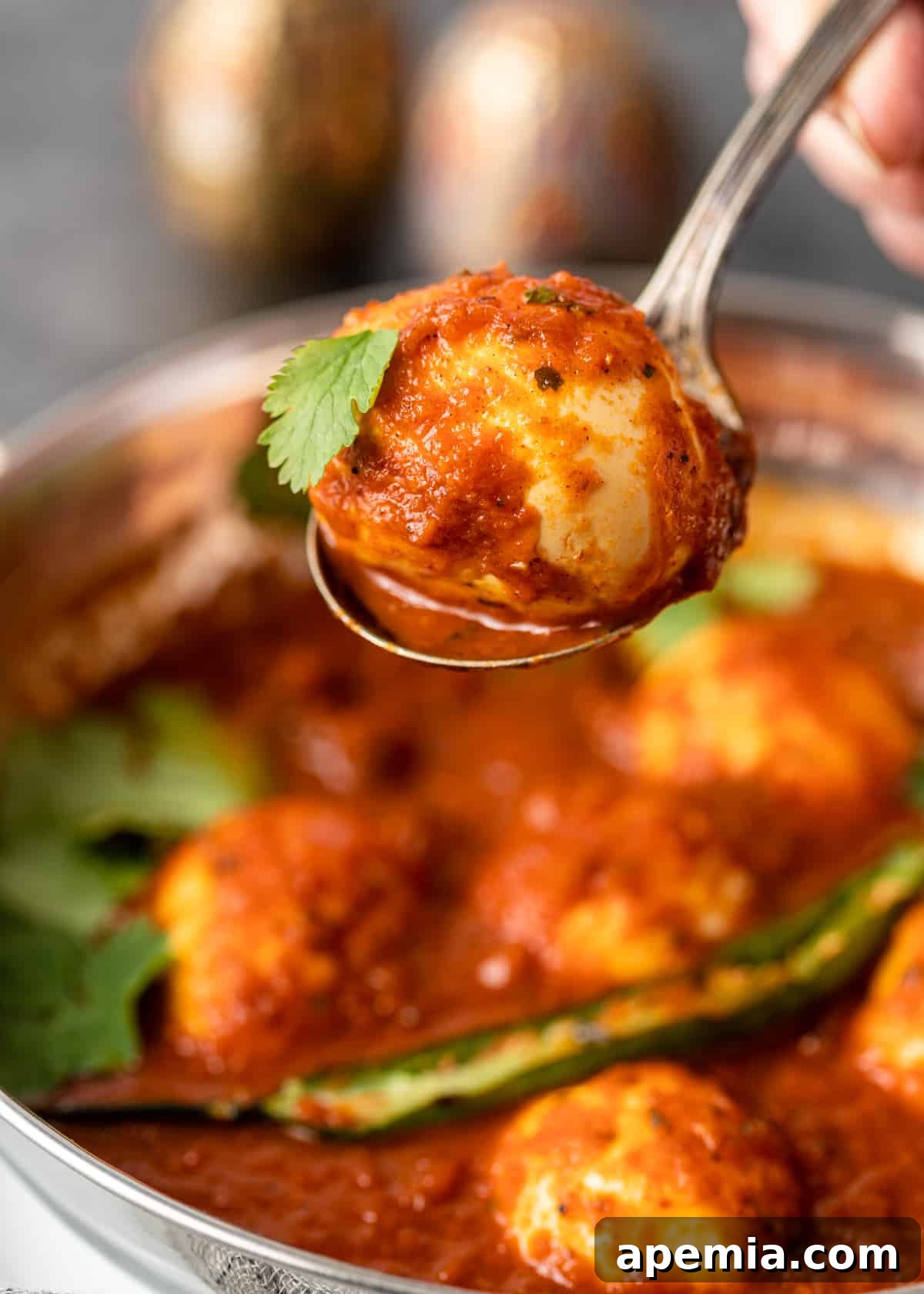 closeup: hand holding spoon of egg curry over top of pot 