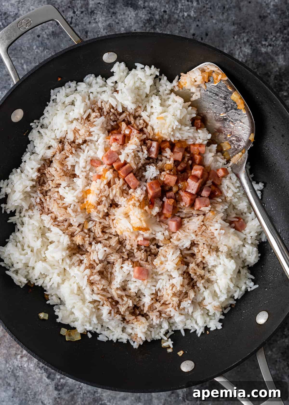 Process shot: A stream of sauce mixture being poured over the rice and fillings in the wok, preparing for coating.