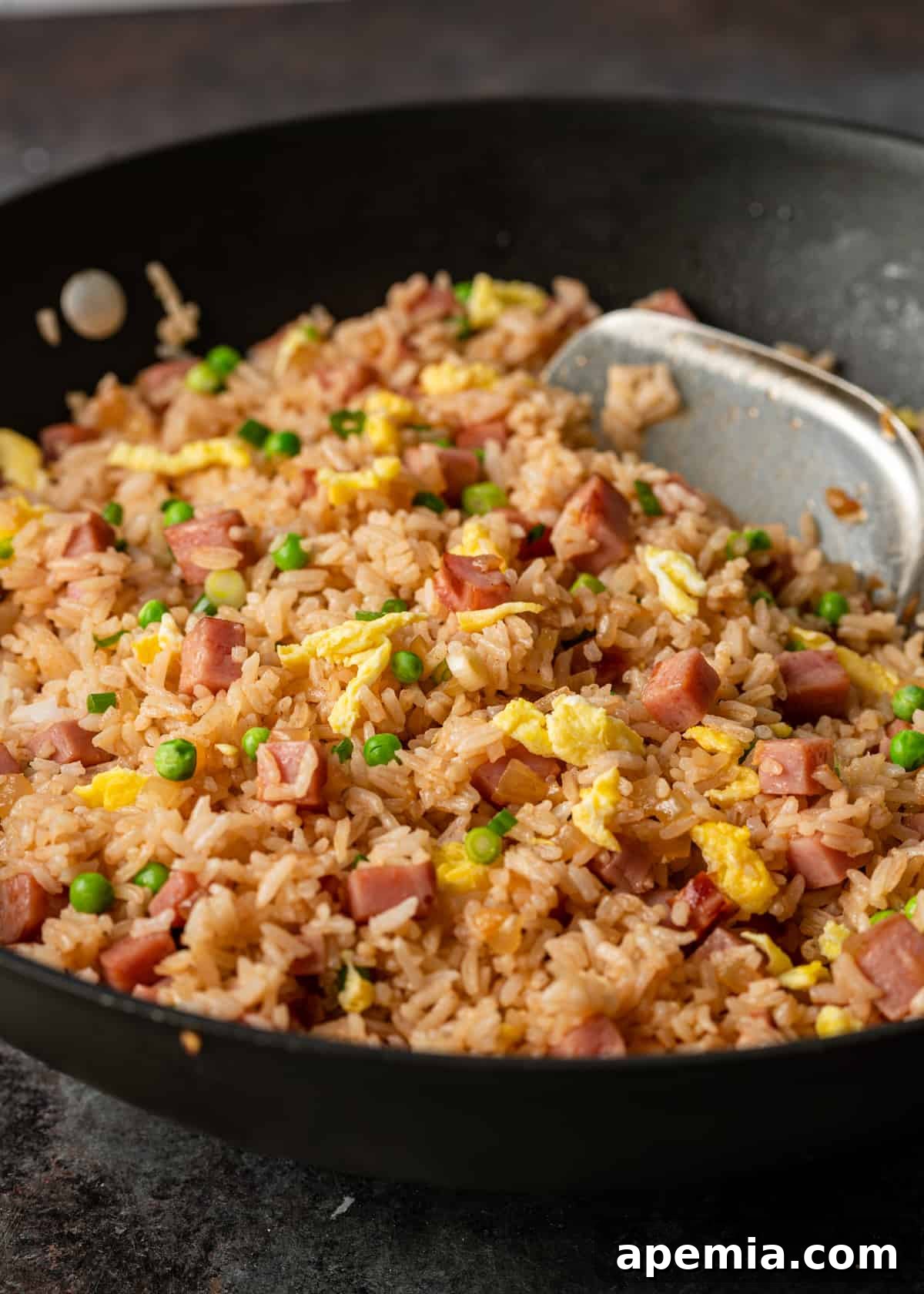 Side view closeup of a hot wok filled with freshly made pork fried rice, ready to be served.