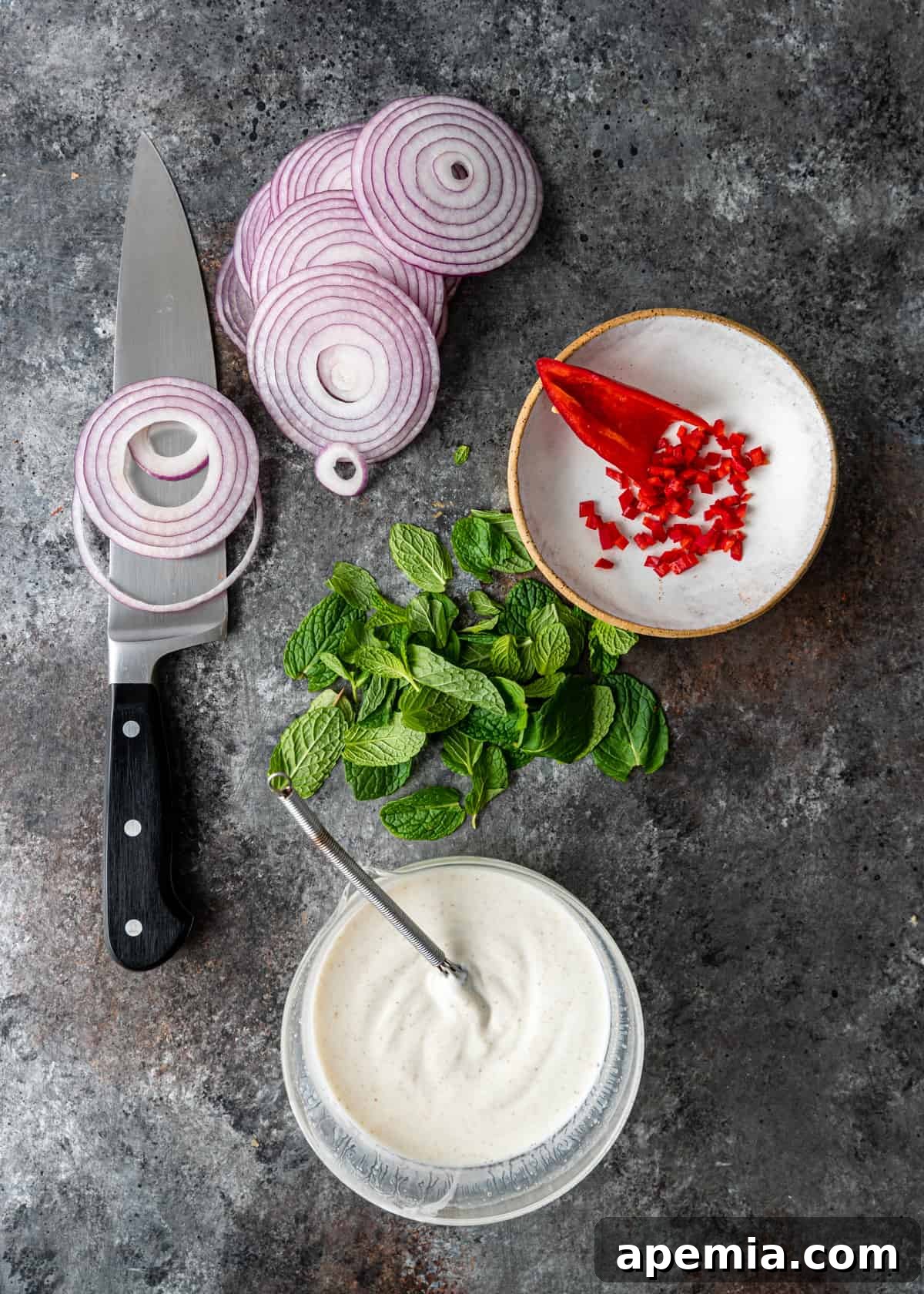 Close-up shot of hands thinly slicing red onions and chili peppers on a cutting board, a crucial step in preparing Onion Raita.