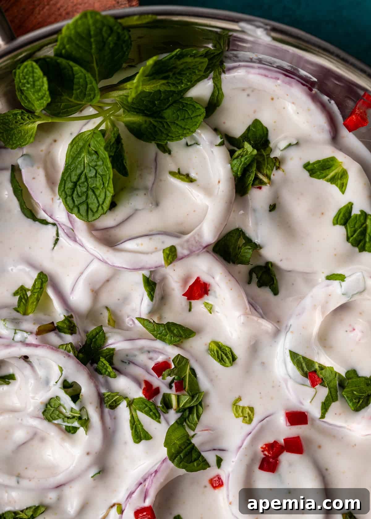 Closeup of Onion Raita in a bowl, showing the texture of the yogurt, onions, and herbs, with a spoon ready for tasting.