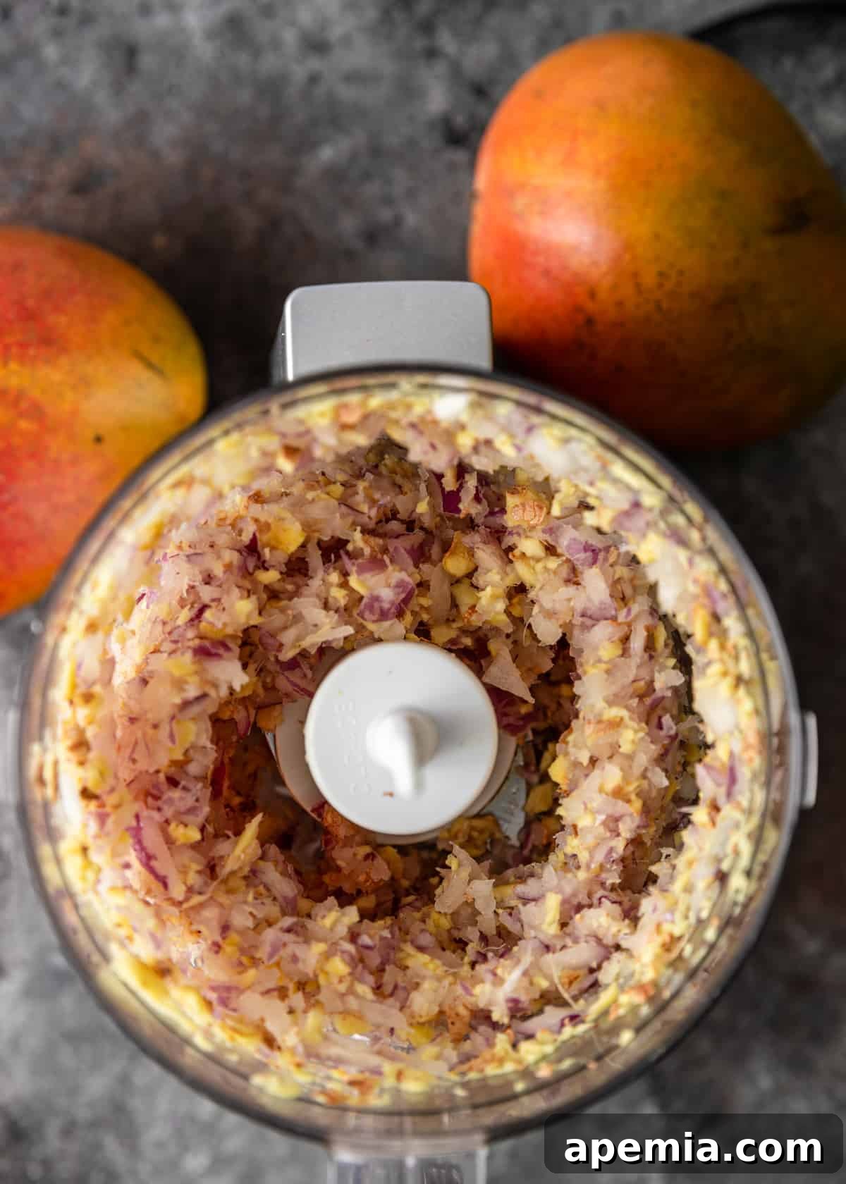 A food processor bowl filled with freshly chopped red onion and grated ginger, ready for the chutney.