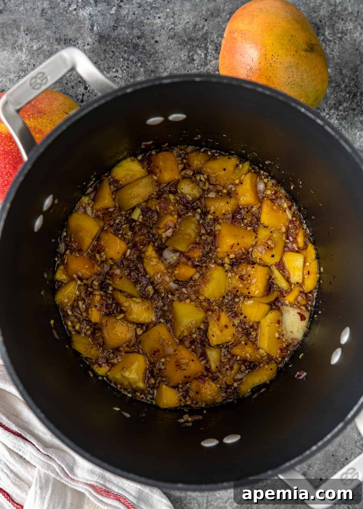 A deep pot showcasing all the uncooked mango chutney ingredients, including mango, onions, spices, and liquid, before simmering.