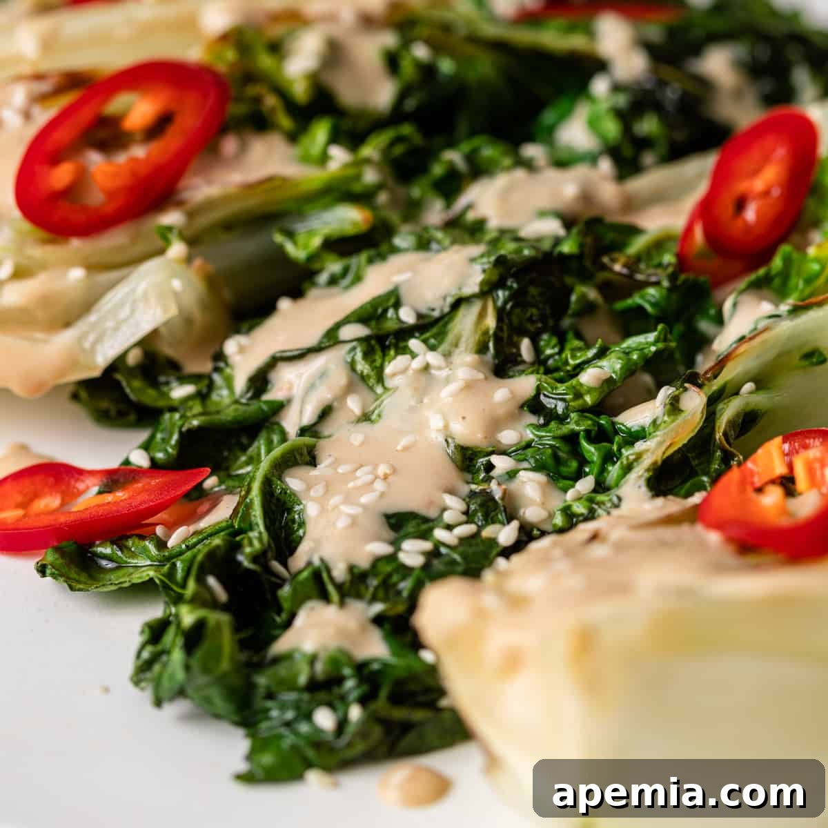 A close up of a vibrant green salad, lightly dressed with a creamy Miso Tahini Dressing, showcasing small red peppers and fresh greens.
