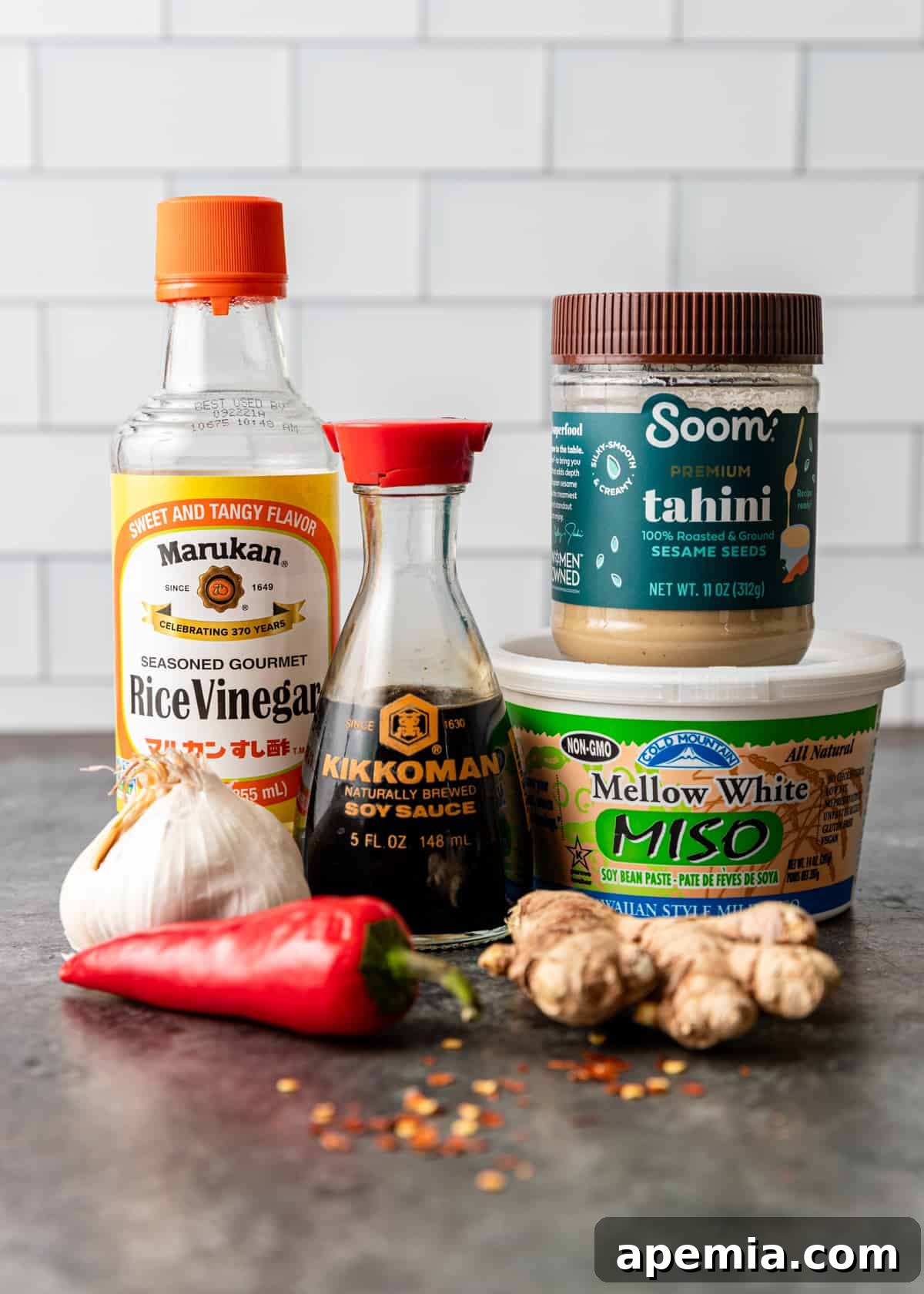 Fresh ingredients for Miso Tahini Dressing, including tahini, miso paste, ginger, garlic, rice vinegar, soy sauce, and red pepper flakes, neatly arranged on a kitchen countertop.