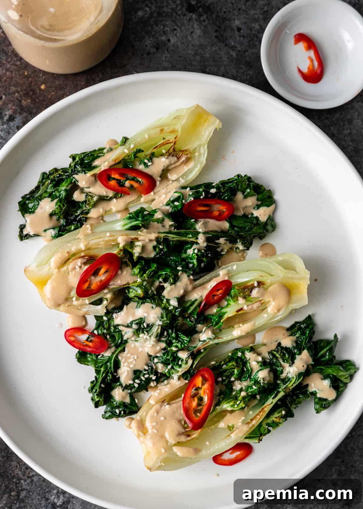 A beautifully composed salad featuring fresh greens and small red peppers, generously coated with a creamy Miso Tahini Dressing, served on a crisp white plate.