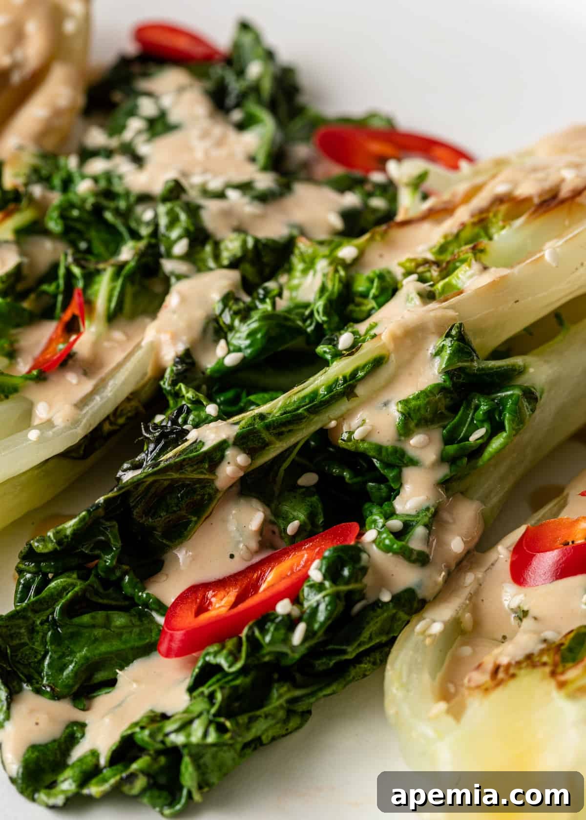 A close up of a fresh salad with vibrant greens and scattered small red peppers, beautifully adorned with a rich and creamy Miso Tahini Dressing.