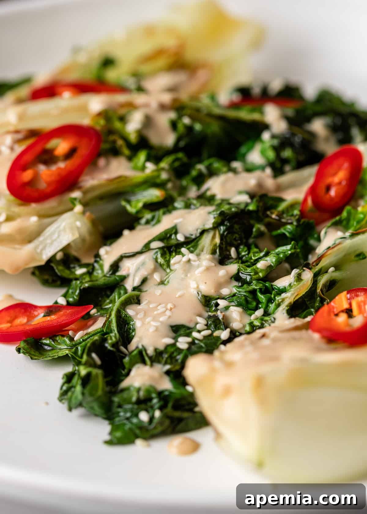 A close up of a fresh, green salad with small red peppers, generously drizzled with the creamy and savory Miso Tahini Dressing.