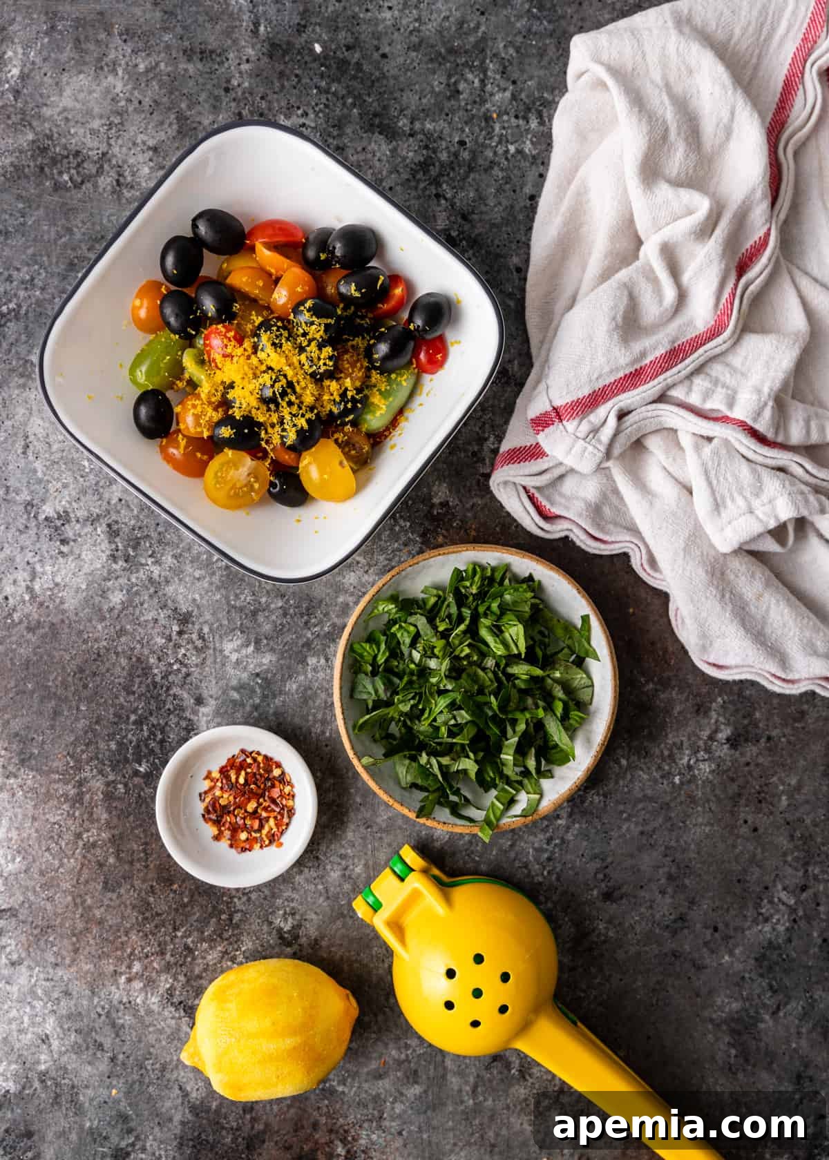 Overhead view of prepped ingredients for Mediterranean cod: sliced cherry tomatoes, minced garlic, lemon zest, and fresh basil.
