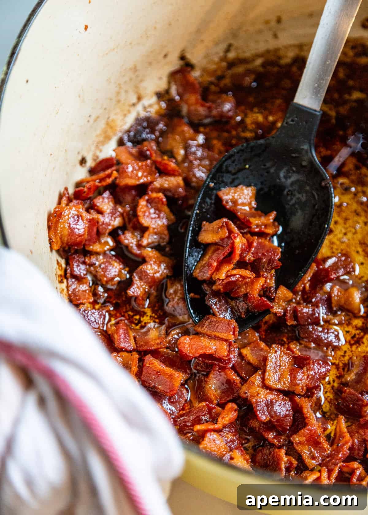 fried bacon in a pot with a large black and metal spoon.