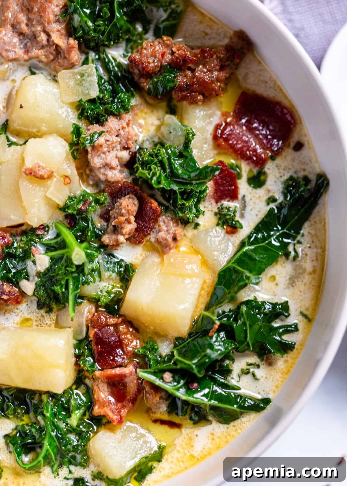 close up of zuppa toscana in a white bowl with potatoes, bacon, and greens visible