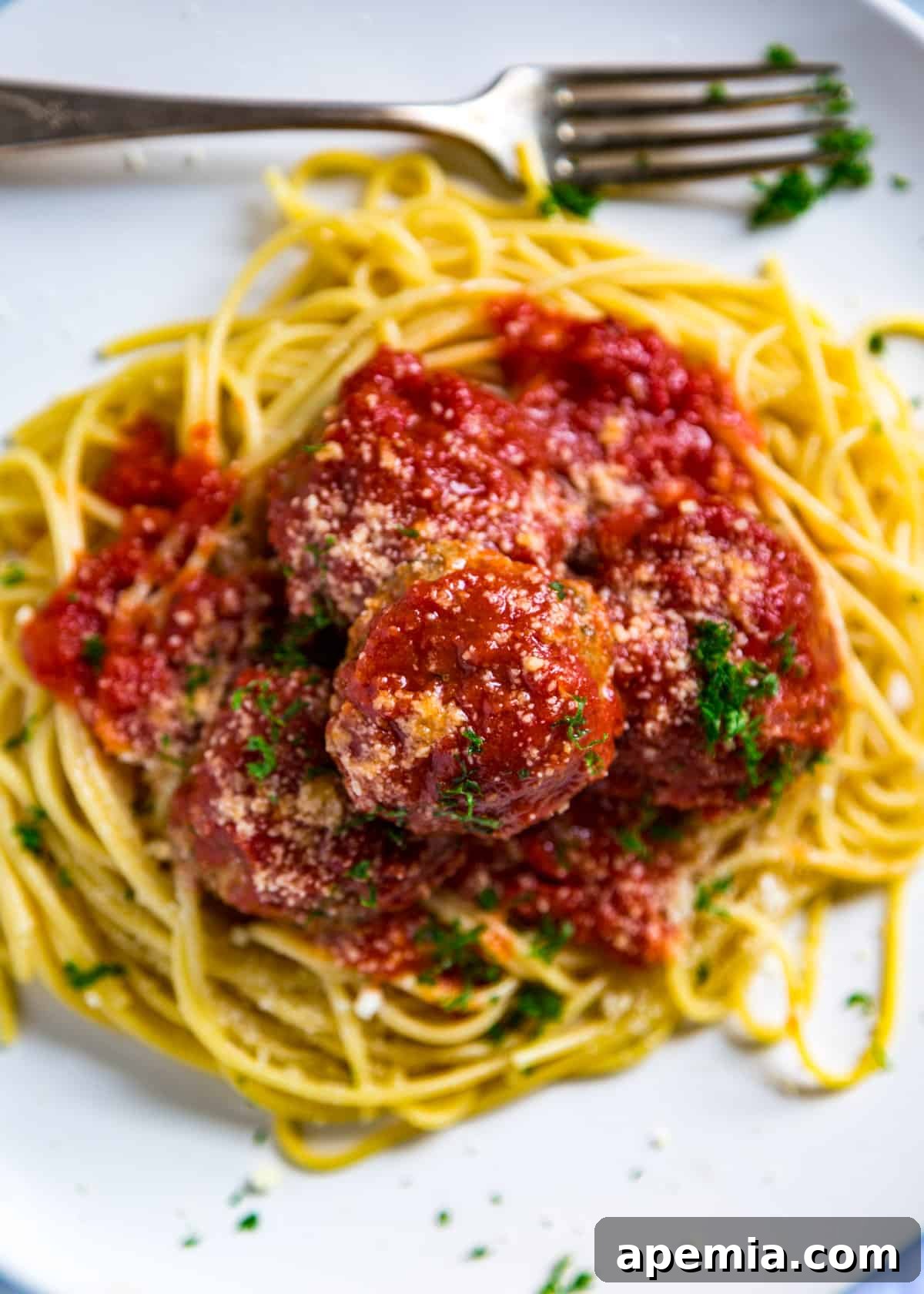 Overhead shot of a full plate of spaghetti generously covered with Italian meatballs, rich marinara sauce, fresh parsley, and grated Parmesan cheese.