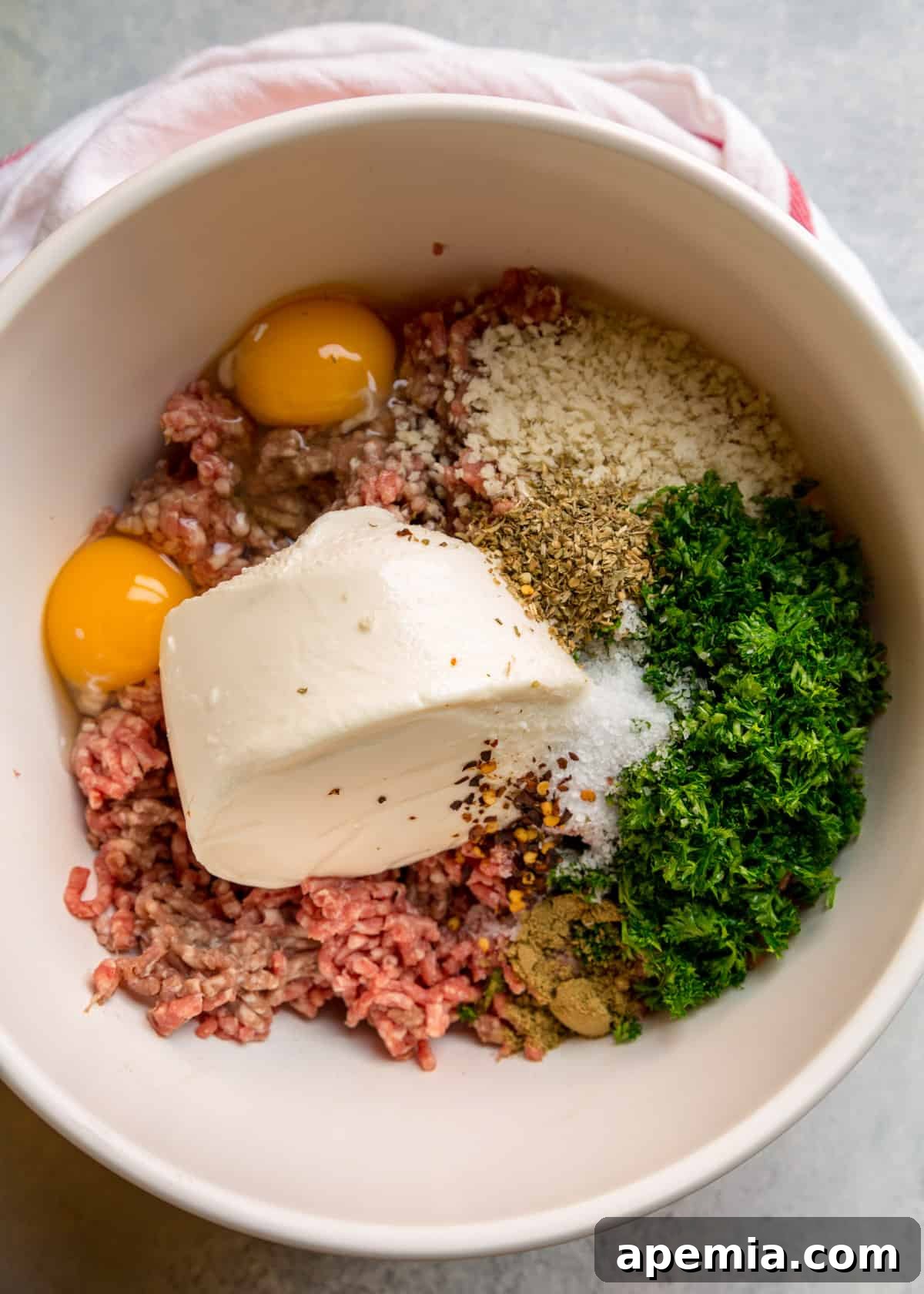 Overhead view of all ingredients for Italian beef meatballs, including ground beef, eggs, cheeses, herbs, and spices, arranged in a large bowl before mixing.
