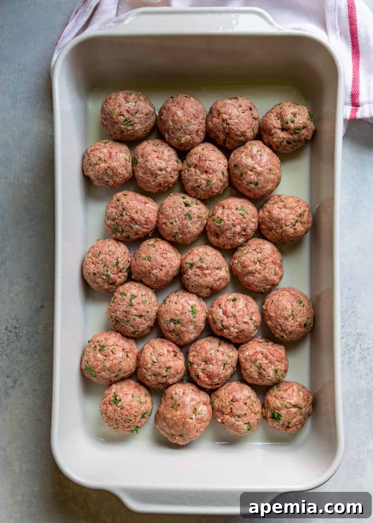 Overhead shot of perfectly formed Italian meatballs nestled closely in a baking dish, ready for roasting.