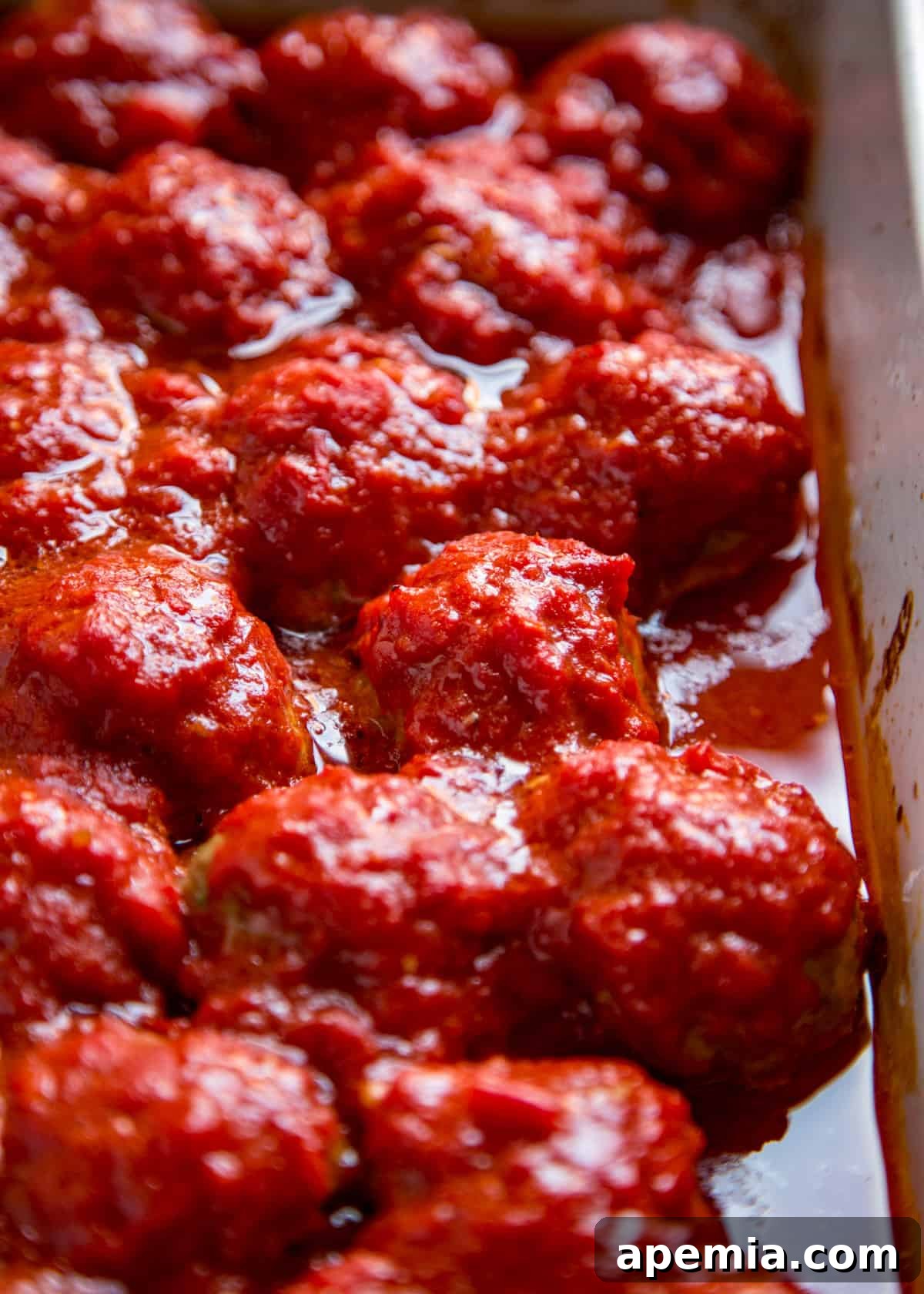 Close-up of roasted Italian meatballs simmering in a rich marinara sauce within a baking dish.
