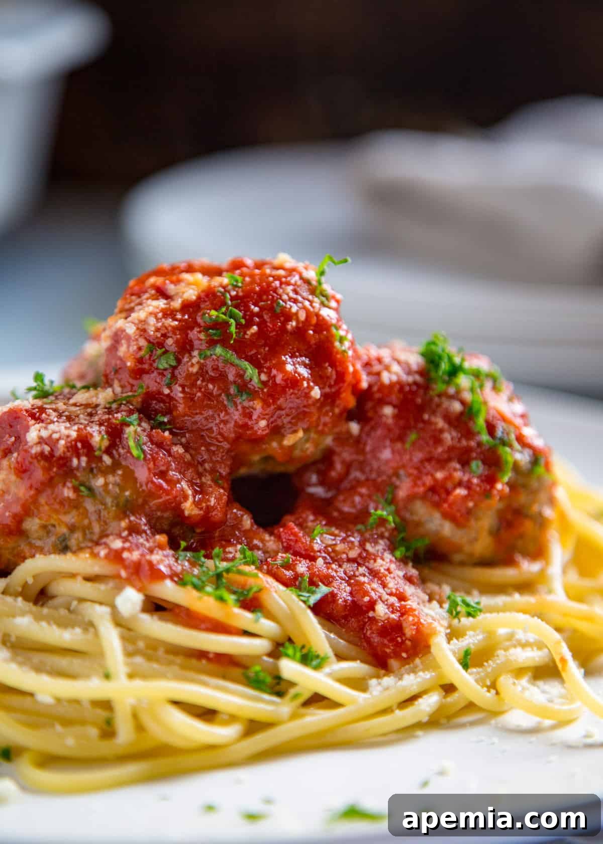 Close-up of a single serving plate with spaghetti topped with three perfectly cooked beef meatballs, vibrant red marinara sauce, and a garnish of fresh parsley.