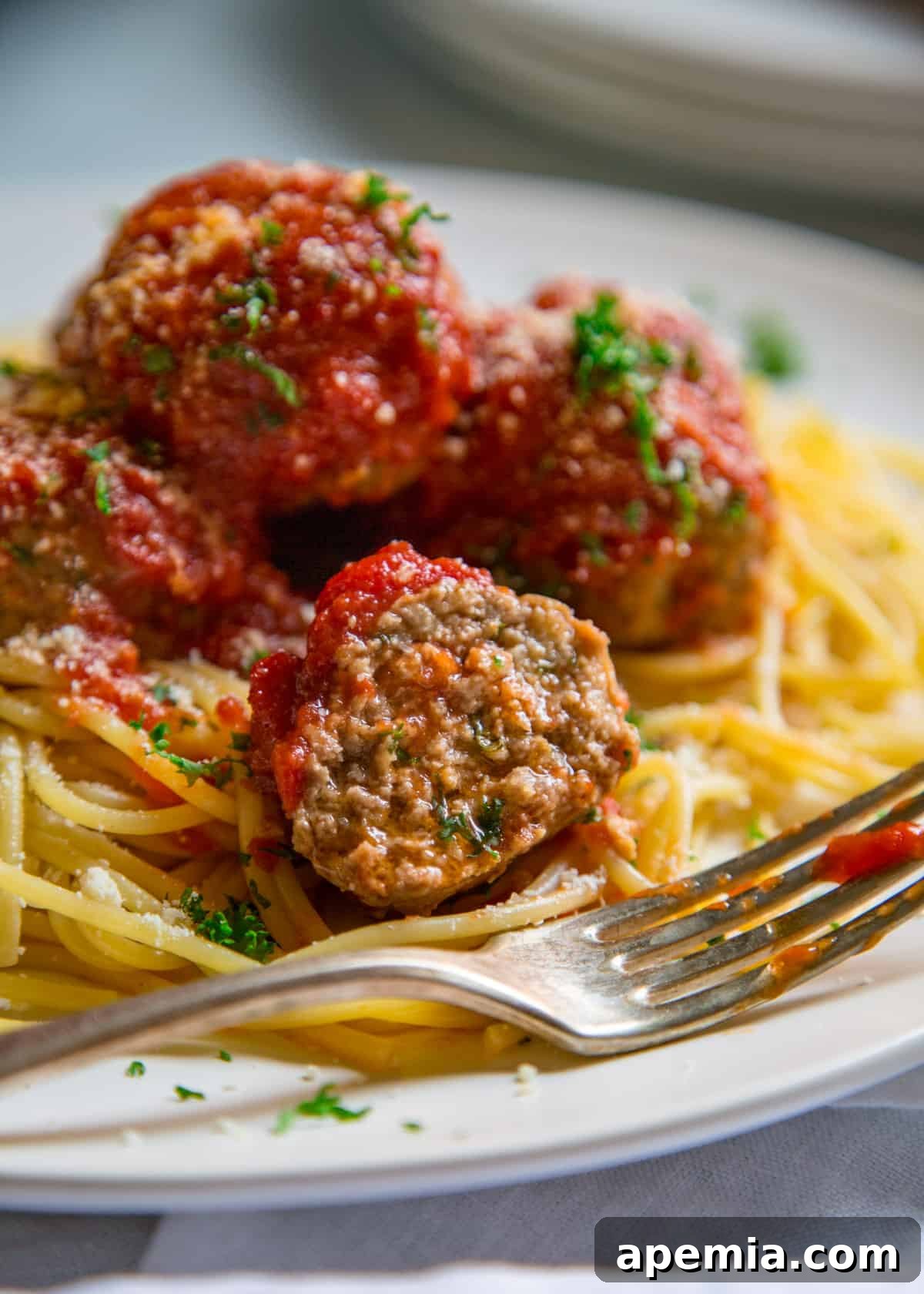 Extreme close-up of a plate of spaghetti with Italian beef meatballs on top. One meatball is perfectly cut in half, showcasing its tender, juicy interior.