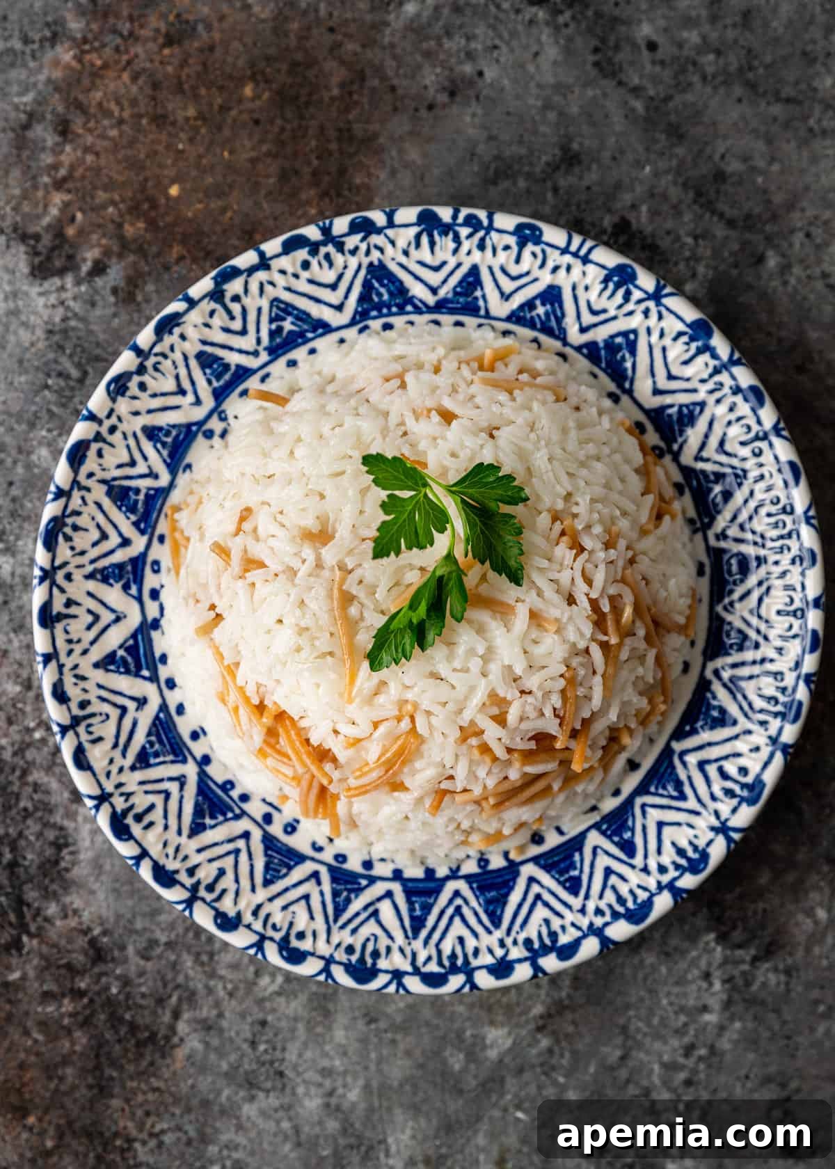 An elegantly plated serving of Egyptian rice with vermicelli, garnished with fresh herbs, on a blue and white dish.