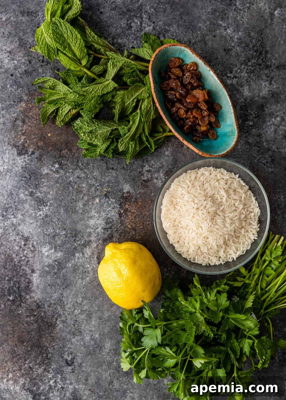 Mediterranean Lamb Lentil Meatballs and Zesty Lemon Rice 5 Overhead shot of fresh mint, parsley, garlic, golden raisins, and olive oil for the mint pesto, alongside jasmine rice and lemon.