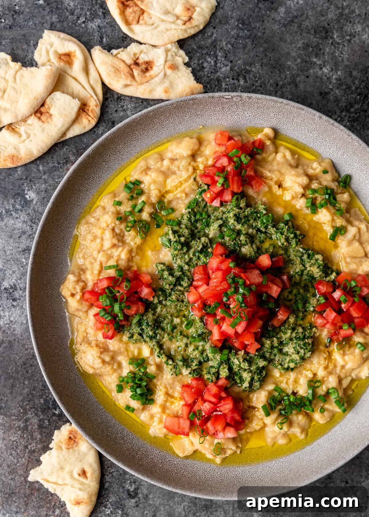 Overhead shot of a platter of Lebanese ful medames, served with warm pita bread and fresh vegetables.
