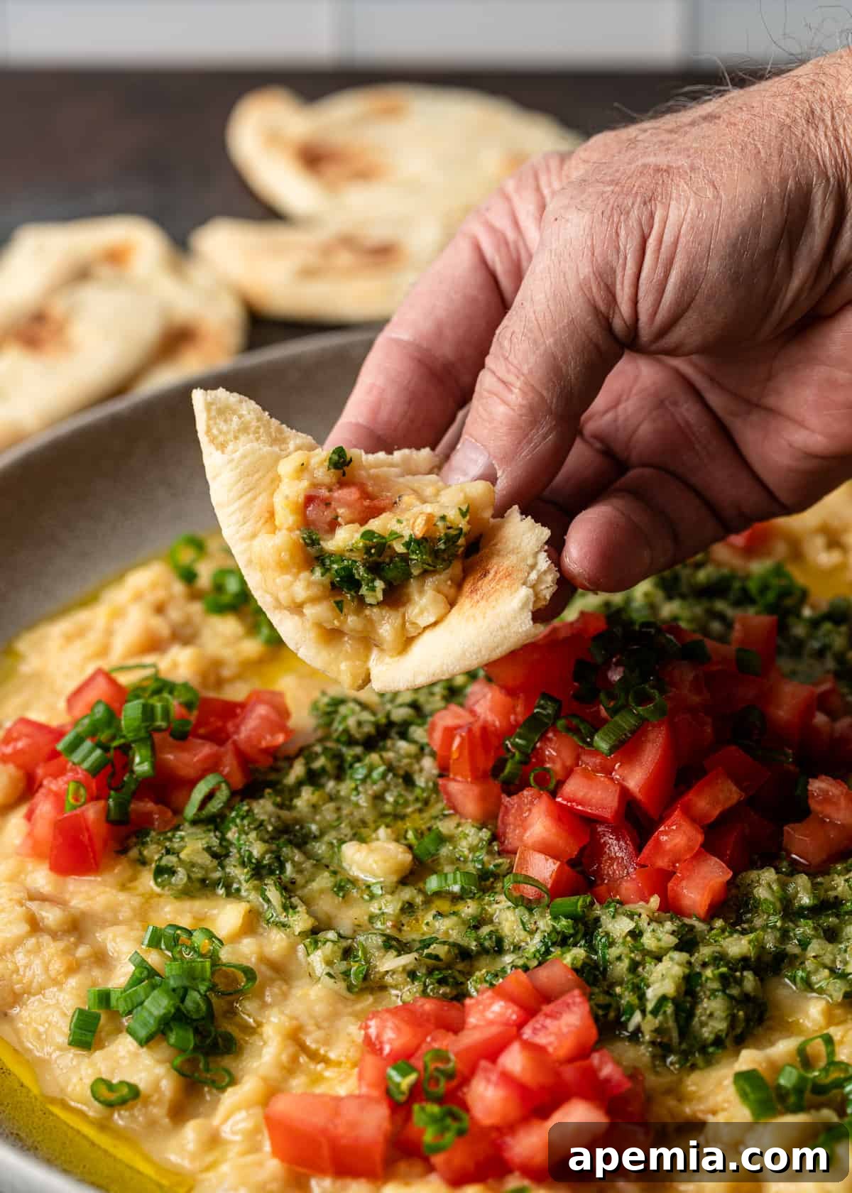 Close-up shot of a hand dipping warm pita bread into a plate of Lebanese ful medames.