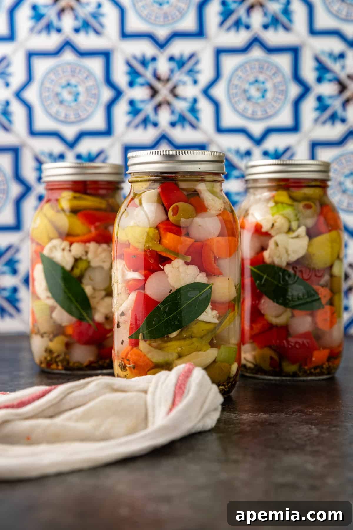 Another perspective of three giardiniera jars on a countertop, emphasizing the vibrant colors of the pickled vegetables.