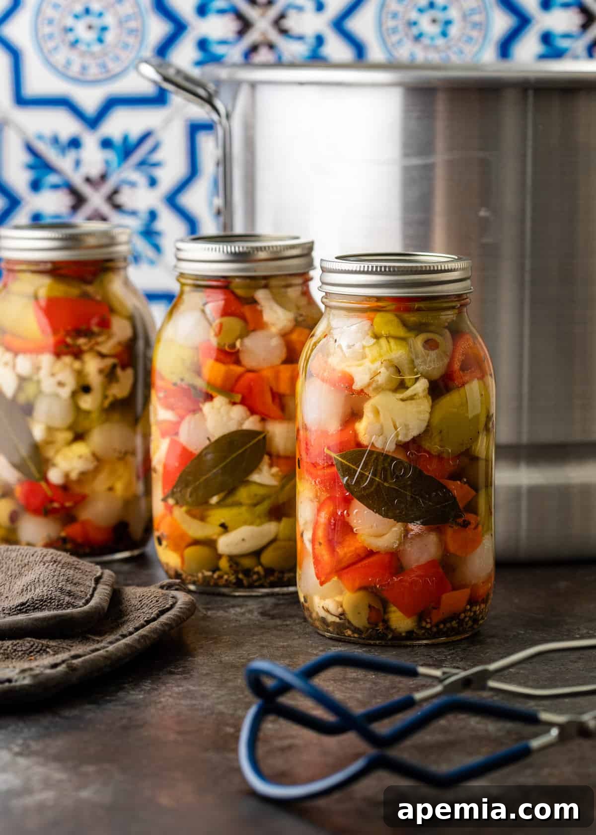 Three beautifully prepared jars of homemade giardiniera stand proudly on a kitchen countertop, showcasing the final pickled product.