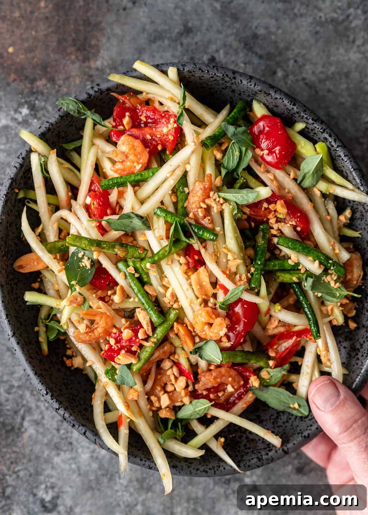 overhead: man's hand holding a bowl of green papaya salad