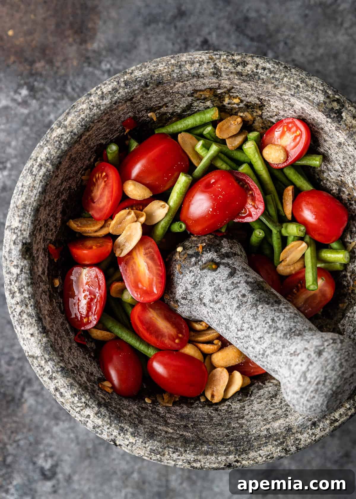 overhead: adding green beans, tomatoes, and peanuts to mortar and pestle