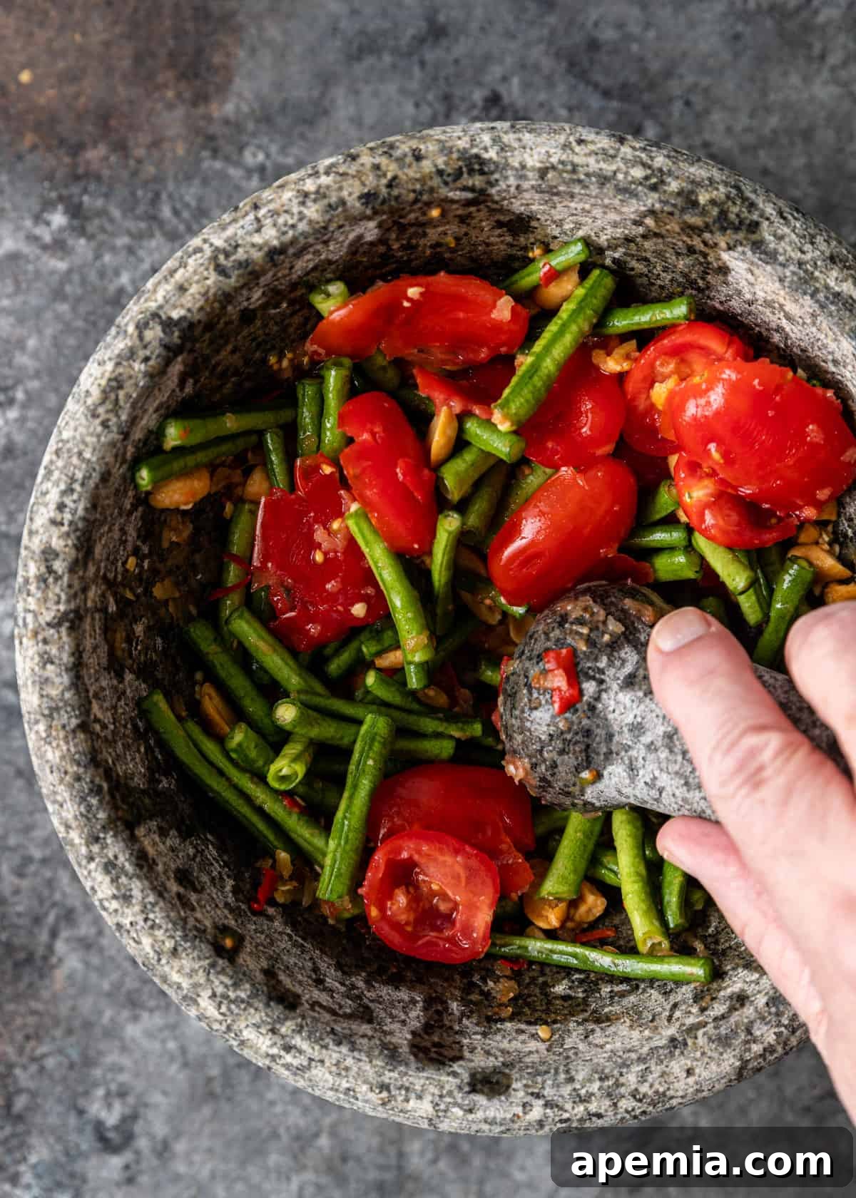 overhead: mashing green beans, tomatoes, and peanuts with mortar and pestle